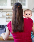 Mother holding baby while working on computer (© Tara Moore/Getty Images)