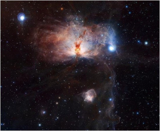 Der Flammen-Nebel im Orion. Das Infrarotbild zeigt sehr gut die wirre, dreidimensionale Struktur der Wolken, mit einer Brücke aus „gelbem“ Gas vor dem leuchtenden Herz des Nebels. Der Pferdekopfnebel ist unten am Bildrand sichtbar, Sigma Orionis ist nur knapp außerhalb des Bildes rechts unten.