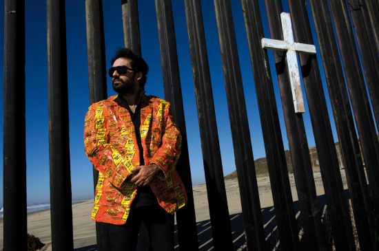 Artist Pablo Llana at the border fence in Playas de Tijuana. The jacket is entirely made from Reese's king size peanut butter cup wrappers. Pablo Llana's art often depicts extreme and unhealthy food consumption in the industrial world. Tijuana, Baja California, Mexico. This picture is part of my long-term project LA FRONTERA: Artists along the US Mexican Border (© Stefan Falke)