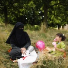 Frau in schwarzer Burka gekleidet sitzt mit einem kleinen Mädchen auf einer Wiese.