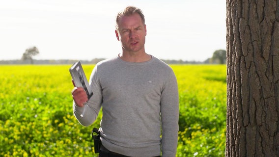 Hinnerk Schönemann mit Buch in der Hand vor einem Feld.  