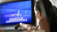 Frau sitzt mit Fernbedienung auf dem Sofa und schaut TV. © Photo_Ma/Fotolia.com Fotograf: Photo_Ma