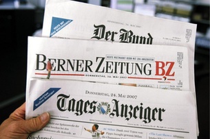 A hand holds up three German-language Swiss newspapers