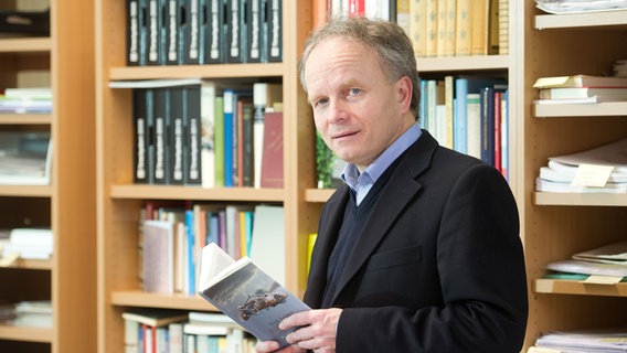 Der Verleger Thedel von Wallmoden mit einem Buch in der Hand vor einem Bücherregal © picture alliance / dpa Foto: Sebastian Kahnert