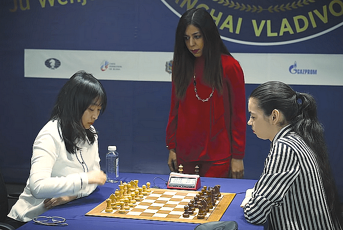 Die amtierende Schach-Weltmeisterin Ju Wenjun (links) schickt sich zum ersten Zug an, gespannt erwartet von ihrer Herausforderin Aleksandra Goryachkina. Im Hintergrund die iranische WM-Schiedsrichterin Shohreh Bayat.