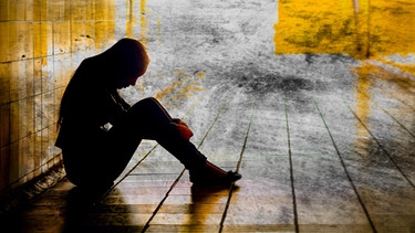 Frau sitzt im Gang mit gesenktem Kopf, abstrakte, gelbe Montage | Bild: colourbox.com