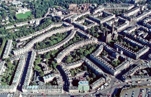 Schottlands Hauptstadt Edinburgh ist doppelgesichtig: neben der Altstadt „Auld Reekie“, der Alten Rauchigen, dehnt sich eine  elegante georgianische Neustadt aus.

Die alte Stadt besteht wesentlich aus einer einzigen Strasse, der „Königlichen Meile“. Sie verbindet die grimmige Burg am oberen Ende mit der Abtei und dem Palast von Holyroodhouse am unteren Ende eines Felskamms. Die Burg taucht au dem Dämmer der schottischen Frühgeschichte auf, den Bau des Palastes begann der Grossvater Maria Stuarts, Jakob IV., um 1500. In der Zeit englischer Invasionen oder bei Bruderzwisten zwischen König und der Nobilität in den Highlands befahl in Burg und Palast nicht notwendigerweise die gleiche Partei. Baugrund innerhalb der Stadtmauern war knapp. Die Hauptstrasse säumten vor allem Mietshäuser, sechs– bis zehngeschossig, damals so gut wie Wolkenkratzer, die Dächer gespickt mit Schornsteinen. Deren Russ und der Rauch der Kochstellen schwärzten die Mauern der Altstadt und verhalfen ihr unter den Edinburghern zu dem Kosenamen „Auld Reekie“. „Reeky“ mahnte in erster Linie die Verrussung und Verrauchung an, Kloakengeruch war allerdings immer mitgemeint. In diesem Stadtorganismus war die Königliche Meile das Rückgrat für Handel und Wandel; gleichzeitig fungierte sie freilich auch als sein Darm. Sie nahm Kot und Kehricht auf.

Die Realunion von l707 machte aus Schottland und England das Vereinigte Königreich Grossbritannien. Von nun an konnte das übervölkerte Edinburgh ungefährdet über die schützenden Stadtmauern hinauswachsen. Der Einstuz eines Mietshauses in der alten Stadt wirkte als Signal, der Plan einer neuen Stadt nördlich der alten nahm Gestalt an. Der Architekt James Craig, unbekannt und gerade mal 22 Jahre alt, gewann 1767 die Ausschreibung und machte sich unverzüglich ans Werk. Auf das Chaos der alten Stadt antwortete er im ersten Quartier der Neustadt mit einem strengen Schachbrettplan. Der Bau der New Town zog sich über ein volles Jahrhundert hin. Der westliche Teil um die Episkopalkirche St. Mary’s Cathedral – unser Bild – wurde erst in den 1880er Jahren 
fertig gebaut. Während dieser ganzen Zeit rührten die Architekten nicht an der pedantisch-eleganten Geometrie der klassizistischen Hausfassaden; die zusammengebauten Häuser kopieren fast zwanghaft das georgianische Muster. Dagegen traten die Urbanisten allmählich etwas lockerer auf. Sie nahmen Rücksicht auf das Gelände; die Häuserreihen bilden nicht mehr nur Quadrate und andere Vierecke, sondern auch Ellipsen, Halbmonde und Kreise. Man denkt natürlich an englische Städte, etwa an Bath; solche „crescents“ und „circuses“ im Stadtbild gehörten damals zum gängigen urbanistischen Vokabular. So löste ein stadtplanerischer Akt von hoher organisatorischer Disziplin das organische Wuchern der alten Stadt ab. In der Geschichte der europäischen Stadt belegt Edinburghs New Town ein Sonderkapitel. Die Auszeichnung als Welterbe im Jahr 1995 galt Edinburgh wohl vorwiegend als einem Beispiel georgianischer Stadtplanung, unübertroffen in Ausdehnung und Erhaltung. Die New Town war übrigens schon zu ihrer Zeit ein voller Erfolg. Magnetisch zogen die neuen Wohnquartiere die betuchten Edinburgher an. Es ist zu vermuten, dass diese nicht nur vor einstürzenden Häusern, Rauch und Russ Reissaus nahmen, sie hatten doch wohl schon lange die Nase voll, buchstäblich. Nach dem Auszug der bemittelten Bevölkerung vergammelte die Altstadt zeitweilig.

Nur nebenbei: auf sieben Hügeln erbaut, hätte Edinburgh den Vergleich mit Rom suchen können. Es wollte aber partout das Athen des Nordens sein. Ein Ehrenmal für die in den napoleonischen Kriegen gefallenen schottischen Soldaten und Matrosen sollte die Gestalt des Parthenons erhalten. Der ehrgeizige Bau begann 1822 auf dem Calton Hügel, aber die Finanzierung kam ins Stottern, der schottische Parthenon brachte es kläglich auf gerade zwölf Säulen. Das Fragment, jetzt als schottisches Nationaldenkmal im touristischen Angebot, erinnert zumindest an den Tod überbordender Griechenland-Begeisterung – und an die wirtschaftliche Realität des knappen Geldes, die ja den sprichwörtlich sparsamen Schotten ein Denkmal wert sein muss. – Aufnahmejahr des Flugbilds: 1999. (Copyright Georg Gerster/Keystone)
