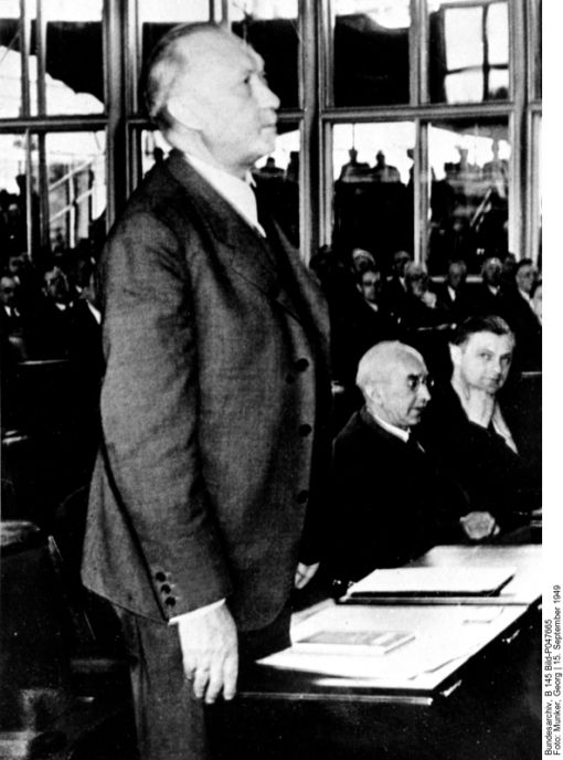 Konrad Adenauer Mit einer Stimme Mehrheit (der seinen) wählt der deutsche Bundestag Konrad Adenauer zum ersten Bundeskanzler der Bundesrepublik Deutschland. 402 Abgeordnete waren stimmberechtigt. Adenauer erhielt 202 Stimmen. Zwei FDP-Abgeordnete waren nicht anwesend, fünf Abgeordnete der CDU/CSU/FDP/DP-Koalition hatten nicht für ihn gestimmt. Dafür votierte der Abgeordnete der Bayern-Partei für ihn – ebenso er selbst. Erster Oppositionsführer wurde der SPD-Vorsitzende Kurt Schumacher. Im Bild: Adenauer erklärt Annahme der Wahl. Rechts im Bild: Franz-Josef Strauss. (Foto: Deutsches Bundesarchiv, B 145 Bild-P047665, 15. September 1949, Fotograf Georg Munker)