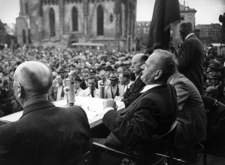 Bundestagswahl 1949 Vor siebzig Jahren, am 14. August 1949, fand die erste Wahl zum deutschen Bundestag statt. Genaugenommen war es der Bundestag der Bundesrepublik Deutschland. In den Augen vieler Zeitgenossen handelte es sich hierbei nur um ein Provisorium.
Aber es erwies sich als erstaunlich haltbar. Zugleich war die erste Bundestagswahl der Beginn einer in dieser Weise nicht vorhersehbaren demokratischen Erfolgsgeschichte. In Anbetracht der vielen alten Nazis, die in der Politik, den Verwaltungen und Hochschulen nach wie vor eine grosse Rolle spielten, hätte es auch anders kommen können.
Die erste Bundestagswahl stand im Zeichen einer starken Polarisierung zwischen SPD und CDU. Die CDU Adenauers strebte eine starke Westbindung an, um unter allen Umständen sozialistische und kommunistische Einflüsse zurückzudrängen. Die SPD unter Kurt Schuhmacher, der von seinem Aufenthalt im Konzentrationslager sichtlich gezeichnet war, tendierte dagegen stark nach links. Entsprechend lautete der Wahlslogan: „Alle Millionäre wählen CDU-FDP. Alle übrigen Millionen Deutsche die SPD.“
Doch damit hatte die SPD nicht den Erfolg, den sie sich erhofft hatte. Sie gewann nur 29,2 Prozent der Stimmen und war tief enttäuscht. Keiner konnte damals vorhersehen, dass ein solches Ergebnis 70 Jahre später Anlass zu grösstem Jubel wäre.
Das Bild entstand am 3. August 1949 während einer Wahlkampfveranstaltung auf dem Rümerberg in Frankfurt/M mit Kurt Schuhmacher, halbrechts im Bild. (Foto: Keystone/AP/Archiv)