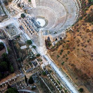 Auf dem Gelände beim türkischen Selçuk wechselten in 7000 Jahren Siedlungsgeschichte ein zeitweilig armseliges Örtchen und eine glanzvolle Weltstadt miteinander ab.

Besiedlungsspuren reichen bis in die Zeit um 5000 v. Chr. zurück. Gross wurde Ephesus als Hafenstadt – musste aber deswegen im Laufe seiner Geschichte immer wieder umziehen, um die Gefahr verlandender Hafenbuchten und versumpfender Ufer zu parieren. Die Einwanderung ionischer Griechen im letzten vorchristlichen Jahrtausend schob die Entwicklung von Ephesus zu einer der reputiertesten Städte an der Westküste Kleinasiens an. Die Stadt beherbergte das Artemision, ein Heiligtum der Göttin Artemis (Diana), das in der Antike zu den sieben Weltwundern zählte. Und als sie kurz nach dem Tod Alexanders des Grossen wieder einmal umziehen musste, war Ephesus schon eine Grossstadt mit 200’000 Einwohnern.

Seine Hochblüte erreichte Ephesus in der römischen Kaiserzeit. als Sitz des Statthalters der römischen Provinz Asia. Die Stadt prunkte mit öffentlichen und privaten Bauten – unter ihnen eine kolossale Marktbasilika, ein Bibliotheksgebäude, Tempel und andere Sakralbauten, ein Versammlungshaus für den Stadtrat, prachtvolle Säulenarkaden und Portale, monumentale Brunnen- und Badeanlagen, luxuriöse Wohnhäuser für betuchte Epheser ebenso wie das Grosse Theater für 25 000 Zuschauer (unser Bild). Zum baulichen Erbe aus der Römerzeit gehören auch Aquädukte und Tunnels zur Fernversorgung mit Brauch- und Trinkwasser. Nach einem zerstörerischen Erdbeben 262 n. Chr. und einem ebenso zerstörerischen Plünderungszug der Goten rappelte sich die Stadt mit Mühe nochmals auf. Erst im Mittelalter büsste sie allmählich Bedeutung und Prosperität ein und verkam schliesslich zu einem blossen Ruinengelände im Osmanischen Reich.

In Ephesus gedieh eine der ersten christlichen Gemeinden. Der Apostel Paulus machte dort auf dem Rückweg von seiner zweiten Missionsreise erstmals Halt und verbrachte später Jahre in der Stadt, zum Teil im Gefängnis. In Ephesus verfassste er die Mehrzahl seiner Briefe, auch einen an die Epheser. In seinen Predigten las er offenbar unter anderem auch den Devotionalienhändlern, die Artemis-  Souvenirs verkauften, die Leviten. Die Silberschmiede, die angesichts schwindender Verkäufe ihr Gewerbe bedroht sahen, demonstrierten im Grossen Theater mit dem Kriegsruf: „Gross ist die Diana der Epheser!“ Ephesus wurde trotzdem ein christlicher Wallfahrtsort. Gemäss der Legende lebte die Gottesmutter Maria vor ihrer Himmelfahrt an der Seite von Johannes in Ephesus. Johannes baute ihr ein Haus. Maria wurde später mit einer Kirche geehrt; über dem angeblichen Grab von Johannes entstand am Hügel von Selçuk die Basilika, die jetzt der Ruhm des christlichen Ephesus ist.. In der Marienkirche tagte 431 das dritte Ökumenische Konzil.

Ein britischer Eisenbahningenieur begann 1863 im Auftrag des British Museum nach dem Artemision zu suchen. Selçuk war damals nichts als eine Ansammlung erbärmlicher Hütten  J.T. Wood stocherte jahrelang auf dem Gelände herum. Als er schliesslich am Ende des Jahrzehnts Überreste des einstigen Weltwunders verortet hatte, waren das Interesse seiner Auftraggeber an weiteren Sondierungen erlahmt und die Geldquellen erschöpft. Der Wiener Ordinarius für Klassische Archäologie, Otto Benndorf, sprang 1893 in die Lücke und beantragte bei seinem Cultus-Ministerium die Grabung in Ephesus. Den Zeitaufwand für die Freilegung der Stadt schätzte er auf etwa fünf Jahre. Die „fünf Jahre“ dauerten (mit weltgeschichtlich begründeten Unterbrechungen) bis jetzt mehr als 120 Jahre. Und das Österreichische Archäologische Institut (ÖAI)  wird aller Voraussicht nach weiter eine halbe Ewigkeit dranbleiben.

Als die Unesco Ephesus im Juli 2015 auf die Liste des Welterbes setzte, war die Genugtuung in Wien womöglich noch grösser als in Ankara. Und das mit Recht. Die Wissenschaftler des ÖAI haben aus Ephesus die eingänglichste, besucherfreundlichste Sehenswürdigkeit  Ioniens gemacht, auch dank vielen geglückten Wiederherstellungen nach den Grundsätzen der Anastylose. So wurde etwa die Fassade der Bibliothek des Celsus mit herumliegenden originalen Bauteilen wieder aufgebaut. 1,5 Millionen jährliche Besucher sind die Belohnung dieser bewundernswerten Anstrengung; allerdings ist es möglich, dass bei ihrer Arbeit gestörte Wissenschaftler so viele Besichtiger gelegentlich auch als Strafe verbuchen. Die Auszeichnung als Welterbe gilt einer in jeder Hinsicht beispielhaften Jahrhundertgrabung – vorbildlich bis zu der ausführlichen Berichterstattung darüber im Internet. – Jahr des Flugbilds: 2002. (Copyright Georg Gerster/Keystone)