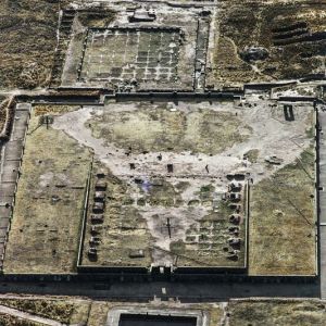 Die Ruinen von Tiwanaku am Südende des Titicaca-Sees
Der Ruinenkomplex von Tiwanaku (vormals zungenbrecherischer Tiahuanaco) liegt nahe dem Südende des Titicacasees auf dem bolivianischen altiplano in über 3800 m Höhe, eine archäologische Fundstätte ungleich jeder andern in Südamerika. Unwirtlicher, kahler, karger geht’s nimmer. Umso erstaunlicher die monumentalen Bauten – oder was eben nach ihrer Nutzung als Steinbruch für La Paz und umliegende Kirchen von einem halben Dutzend Kultanlagen übrig ist. Das noch aufgehende Mauerwerk besteht aus grossen, präzis geschnittenen, mörtellos gefügten Blöcken.

Den Hof eines halb unterirdischen Heiligtums (auf dem Flugbild ganz unten) frieden Wände mit skulptierten Menschenköpfen ein, ein Hinweis auf Kopfjagd. Auf der im Bild anschliessenden Plattform für einen Tempel steht (in der oberen rechten Ecke) das sogenannte Sonnentor, eine Ikone der Vorinkazeit. In dem Puzzle der vorinkaischen Kulturen hat Tiwanaku von jeher die Rolle eines Jokers. Sogar Archäologen zitieren gerne Tiwanaku-Einfluss, wenn eine Leerstelle im Bild einer Regionalkultur zu füllen ist. Und erst die Obskuranten und Spintisierer vom Dienst – für sie ist Tiwanaku ein Geheimnisknochen, den abzunagen sie nicht müde werden: Gegründet wurde es von Götterastronauten schon im Tertirär; 250 000 oder auch nur 25000 Jahre soll es alt sein, die älteste Stadt der Erde. Undsofort undsofort. Möge man sich über solche Phantastereien damit hinwegtrösten, dass ja auch Wissenschaft immer nur der aktuelle Stand unseres Unwissens ist – und Tiwanaku gibt zweifellos mehr Fragen auf, als es gesicherte Antworten zulässt.

Siedlungsspuren hier sind wenigstens dreitausend Jahre alt. Aber erst als die Dörfler die Enge ihrer ökologischen Nische mit verbesserten Anbautechniken für Kartoffeln, Bohnen und Quinoa sprengten und Agrarüberschüsse erzeugten, erblühte Tiwanaku im ersten Jahrtausend n. Chr., zwischen 300 und 900, zu einem religiösen und kulturellen Zentrum des südlichen Andenraums. Auch politisch entwickelte es Ambitionen. Es dominierte das heutige Bolivien und darüber hinaus den Nordwesten Argentiniens, das nördliche Chile und das südliche Peru.

Die Forschung sieht zunehmend Tiwanaku als Kapitale eines ersten Grossreichs in den Anden – auch wenn dieses Gebilde kaum die straffe Bürokratie des späteren Inkareichs vorwegnahm. Tiwanaku wurde im Jahr 2000 Welterbestätte. Bolivien setzte in letzter Minute durch, dass Tiwanaku entgegen dem ursprünglichen Antrag ausdrücklich nicht nur als spirituelles, sondern auch als politisches Zentrum (mit einst bis an den Pazifik reichender Macht) gewürdigt werde. Schon möglich, dass es damit einfach die archäologische Neuorientierung nachholte. Aber vielleicht ist die Umbenennnung auch eine Botschaft durch die Blume an Chile und Peru: der isolierte Andenstaat Bolivien kann den Verlust von Küste und Meer (1884, nach dem Salpeterkrieg) nicht verschmerzen. – Jahr des Flugbilds: 1994 (Copyright Georg Gerster/Keystone)