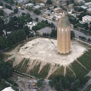 Der Grabturm Gonbad-e Qabus im Nordosten Irans
Während in Timbuktu bigotte Bilderstürmer dabei waren, als Welterbe geschützte Mausoleen ihrer sufistischen Glaubensbrüder im Namen islamistischer Rechtgläubigkeit zu demolieren, erweiterte die Unesco in einer Sitzung in St. Petersburg das Inventar der Welterbestätten um 26 neue Natur- und Kulturgüter.

Unter diesen ist auch der Grabturm Gonbad-e Qabus im nordöstlichen Iran. Dem Gonbad („Kuppelbau“) dient ein eingeebneter prähistorischer Siedlungshügel als Sockel. Der 52 Meter hohe und hohle Turm stand einst isoliert in der Turkmenensteppe; heute ist er das Wahrzeichen und der Namensgeber einer modernen iranischen Stadt. Kein anderer Grabturm in Iran ist höher oder besser erhalten. Der sich leicht verjüngende Rundturm mit konischem Dach, erbaut mit gelben gebrannten Ziegeln und mit Risaliten gerippt, entbehrt jeden Schmucks.

Zwei identische Inschriften nennen das Baujahr – in die christliche Ära umgerechnet: 1006/1007 n. Ch. – und den Grabherrn, den für seine Grausamkeit berüchtigten Emir Shams al-Maali Qabus ibn Voshmgir. Er wurde 1012 ermordet und bezog den zu seinen Lebzeiten erbauten Turm in einem Glassarg. Die Grabanlage hätte bei den malischen Eiferern von heute sicher Anstoss erregt. Zwar war der Emir ein strenggläubiger Sunnit, aber offenbar nicht gegen zoroastrische Anfechtungen gefeit.

Der Glasssarg wurde im Turm an Ketten aufgehängt, unter der Kuppel frei schwebend. Keinesfalls durfte nach zoroastrischer Lehre der Leichnam die heilige Erde berühren. Zudem trafen die Strahlen der Morgensonne durch ein strategisch angeordnetes Fenster im Kuppeldach den Toten, Himmelfahrt verheissend. Auch dieses unislamische Arrangement weist vermutlich auf die altiranische Lichtreligion zurück. Aufnahmejahr: 1978 (Coypright: Georg Gerster/Keystone)