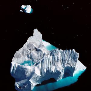  Der Jakobshavn Isbrae Gletscher beschickt durch den Ilulissat Icefjord die westgrönländische Disko Bucht mit Eisbergen: das Naturschauspiel hat auf der Nordhalbkugel nicht seinesgleichen.

Die Unesco billigte 2004 dem 40 Kilometer langen Eisfjord die Bedeutung von Weltnaturerbe zu. Die Auszeichnung gilt nicht dem  Eiskanal allein, sondern der ganzen Naturveranstaltung um das Fischerdorf Ilulissat („Eisberg“ auf grönländisch). Der Jakobshavner Gletscher, eine Zunge des grönländischen Inlandeises, hat es eilig. Statt zu kriechen rennt er – bis zu 35 Meter pro Tag. An der Abbruchkante kalbt er täglich grosse und kleine Eisberge. Die grossen bleiben mitunter für Wochen oder sogar Jahre in dem engen Eiskanal stecken, bis sie von dem nachrückenden Eis weiterbugsiert oder zermalmt werden. Die kleinen erreichen unbehindert die Disko Bucht, von wo sie ins offene Meer driften. Die Absenderadresse des Eisbergs, der die Titanic versenkte, hiess Ilulissat

Satelliten haben ein wachsames Auge auf den Gletscher, sie messen unablässig nach. Zwischen 1997 und 2003 verdoppelte er seine Geschwingkeit auf  jährlich 9,4 Kilometer. Wenn er es so eilig hat, beliefert er den Atlantik jährlich mit 30 Milliarden Tonnen Eis – genügend für einen messbaren Anstieg des Meeresspiegels.

Sommers machen tausende unterfütterte Schlittenhunde an Ketten Ilulissat unsicher; dafür ist die Aussicht auf die Disko Bucht mit tausenden schwimmenden Eisbrocken jeder Grösse lieblich wie sonst nie. Blaue Schmelzwassertümpel schmücken die Eisberge wie eingesetzte Saphire. Zwischen den Eistrümmern und -bergen navigieren Ausflugsboote. Annäherungen sind nicht ganz ungefährlich. Die frei schwimmenden Eisberge sind in prekärem Gleichgewicht. Unversehens verlieren sie es, taumeln, rollen, wenden, überschlagen sich – und verursachen dabei Mini-Tsunamis mit zerstörerischen Wellen in der ganzen Bucht.

Ilulissat ist schon heute der meistbesuchte Ort Grönlands. Seit kürzlich der Weltkongress der Weihnachtsmänner in Kopenhagen Grönland als die wahre Heimat von Santa Claus anerkannt und das Tourismusbüro von Ilulissat den Briefkasten von Santa Claus übernommen hat, und bereit ist, an seiner Stelle abertausand Kinderbriefe aus aller Welt zu beantworten, stützt noch das Märchen die Attraktion des Naturwunders. – Jahr des Flugbilds: 1989 (Copyright Georg Gerster/Keystone)