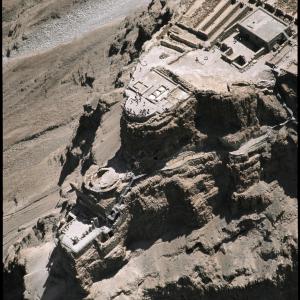 (Copyright: Georg Gerster/Keystone)

 Der Festungspalast des Herodes ist das Herzstück des Masada Nationalparks. Masada war lange das von keinem Zweifel angekränkelte Wahrzeichen für Israels Selbstbehauptungswille.

Sonderbar: Der Felsklotz unweit des Toten Meers, ein natürlicher Burgberg, wenn es je einen gab, geriet erst spät, sehr spät in den Lichtkegel gesicherter Geschichte. Ein hasmonäischer Priesterfürst nützte erstmals nach 104 v. Chr. den Fels als Festung. Seinen grossen Auftritt hatte Masada aber erst unter König Herodes (73-4 v. Chr.). Dieser errichtete auf der Gipfelfläche des Felsens Kasernen, Wohn-und Verwaltungbauten, Bäder und Lagerräume; absteigend über drei Stufen, die eine überdachte Treppe untereinander verband, entstand an der Nordspitze ein „hängender“ Palast, Winterresidenz des Königs. Vor allem aber befestigte er Masada mit Kasemattenmauern sowie 38 Wachttürmen und legte in deren Schutz Waffenarsenale, Vorräte an Getreide, Datteln, Hülsenfrüchten, Wein, Öl und Wasser an.

Der König, praktizierender Jude, aber arabischer Abstammung, misstraute seinen jüdischen Untertanen ebenso wie seinen römischen Oberherren (mit Grund: so blickte etwa Kleopatra, die Mätresse des Antonius, begehrlich auf das Königreich Juda); ein wehrhaftes Refugium, eine Fluchtburg kam ihm und seiner Familie zustatten. Nach Herodes’ Tod erhielt Masada eine römische Garnison. Als Auftakt zu dem ersten jüdischen Aufstand gegen Rom bemächtigten sich im Jahr 66 die Zeloten, eine ultranationalistische jüdische Partei mit einem terroristischen Flügel, den Sikariern („Dolchmännern“), der Festung. Sie hielten sich dort auch nach der Eroberung Jerusalems und der Zerstörung des zweiten Tempels verschanzt. Als die Römer im Jahr 72 zur Belagerung Masadas schritten, lebten angeblich 967 Menschen auf dem Berg, lauter Sikarier und ihre Familien (so jedenfalls die einzige Quelle, der zeitgenössische jüdische Geschichtsschreiber Flavius Josephus).

Die Belagerer schlossen den Burgberg mit einem Wall ein und bauten eine Rampe, über die sie Sturmböcke und andere Belagerungsmaschinen vor die Festungsmauer brachten. Im Mai 73 schlugen sie eine Bresche und setzten die Holzverschanzung dahinter in Brand. Römischer Gefangenschaft und Sklaverei zog die Besatzung den Tod vor. Ihre Habe verbrannten sie – nicht aber die Lebensmittevorräte. Die Römer sollten erkennen, dass nicht Hunger sie zu der Verzweiflungstat getrieben hatte. Die Männer töteten ihre Lieben, Frauen und Kinder, und zuletzt gegenseitig sich selber. Nur der letzte nahm es auf sich, die schwere Sünde des Selbstmords zu begehen und sich ins Schwert zu stürzen. Zwei Frauen und fünf Kinder, die sich in einer Wasserleitung verkrochen hatten, überlebten.

Yigael Yadin, General und Archäologe, erforschte Masada, grabend und restaurierend, von 1963 bis 1965. Dem jungen jüdischen Staat wurde es ein Wahrzeichen für Behauptungswillen selbst um den Preis der Selbstaufopferung. Allerdings gab es auch von den zionistischen Erzrvätern Israels immer wieder Widerspruch: war denn Masada nicht ein abschreckendes Beispiel von Defaitismus? Solchen Einwänden und Bedenken zum Trotz vereidigte die israelische Armee jahrelang ihre Rekruten bei Fackelschein auf Masada. „Nie wieder darf  Masada fallen“, schloss die Eidesformel.

An patriotischem Numinosum hat Masada seither eingebüsst. Schon seine touristische Erschliessung als Nationalpark mit jährlich 722 000 Besuchern (2013) hat den Mythos Masada angekratzt: Fast Food und Snacks, Son et Lumière und eine Luftseilbahn, mit der Besucher von der Talstation 257 Meter unter dem Meeresspiegl in 3 Minuten knapp unter das Gipfelplateau 33 m ü.M. schweben, schaffen ein „Masada ohne Tränen“, mit dem sich die Pioniere von einst schwer abfinden. Auch sonst muss der Mythos Masada mit Retuschen leben. Wie zuverlässig ist der Geschichtsschreiber Flavius Josephus, „Roms Lakei“ (Professor Nachman Ben-Yehuda)? Yadin fand jedenfalls auf Masada Skelettreste von nicht mehr als 25 Menschen. Viele Israeli mögen ja ohnedies von Herzen wünschen, dass Flavius Josephus total unzuverlässig ist. Die „Patrioten“ auf Masada waren laut Josephus Sikarier – eine Bande Fanatiker, Terroristen, Desperados und Mörder (vergleichbar den heutigen ISIS-Milizen). Und erst noch dumm genug – so Ben-Yehuda  –, sich in eine Festung einzuschliessen und sich so den Römern, genialen Belagerern, auszuliefern, statt eine Guerilla zu bilden.

Der landschaftliche Rahmen, der bautechnisch kühne Palast des Herodes, eine beispielhaft ausgetüftelte Wasserversorgung, das römische Belagerungswerk, die geschichtliche Bedeutung und Strahlkraft verbürgen Masadas Einzigartigkeit, die Voraussetzung zu einer Würdigung als Welterbe. Aus der Identitätsfindung des Staates Israel ist Masada nicht wegzudenken. Trotzdem kam die Ehrung erst 2001 zustande. Erzürnt über die jordanische Nomination von Jerusalem 1981 und deren Begleitumstände, hatte Israel bis 1999 dem Welterbeprogramm die kalte Schulter gezeigt. – Jahr des Flugbilds: 1972. (Copyright Georg Gerster/Keystone)
