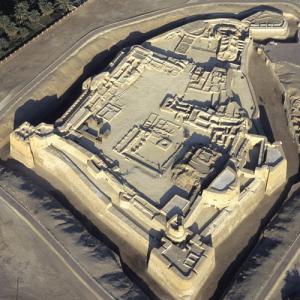 Die Burg von Bahrain
Die portugiesische Burg von Bahrain, Qal’at al-Bahrain, krönt einen 300 x 600 m grossen und 12 m hohen Ruinenhügel (Tell), der während 4500  Jahren, seit der Zeit des Reichs von Dilmun, ununterbrochen besiedelt war. Dilmun hat seinen Auftritt schon in den ältesten sumerischen Keilschifttexten, die zwischen 3300 und 2300   v. Chr. in Tontafeln eingeritzt wurden, und es bleibt in Mesopotamien bis in die neubabylonische Zeit ein Begriff.

Dilmun monopolisierte den Seehandel zwischen dem Industal und dem Zweistromland. Zeitweilig geriet es offenbar in Abhängigkeit von Stadtstaaten am Euphrat oder Tigris. Seine Bedeutung übersteigt die eines erfolgreichen Handelsplatzes. Dilmun ist Teil des sumerischen Schöpfungsmythos. Im Gilgamesh-Epos figuriert Dilmun als das Paradies.

Die Angaben in Textquellen zu seiner Lage und Ausdehnung indes sind verwirrlich und widersprüchlich; Dilmun war lange schattenhaft, kaum mehr als ein Gerücht. Schon früh vermuteten freilich die Forscher, dass die Insel Bahrain, einst gesegnet mit artesischen Süsswasservorkommen, das Dilmun-Paradies sein könnte. Aber erst 1954 - 1970  nahmen sich dänische Archäologen den Tell bei Manama, der Hauptstdt des Königreichs Bahrain, vor. Und sie entdeckten, dass tatsächlich seine ältesten Schichten von 2200 v.Chr. zur Dilmun-Kultur gehören, das Gerücht war endlich dauerhaft verortet.

Auch jüngere Besiedlungsbelege aus nahezu zwei Jahrtausenden wiesen die Ausgräber der Dilmun-Kultur zu: Monumentalbauten an einer Prachtstrasse, Repräsentations-, Wohn- und Vorratsräume eines Palastes, ein Tempel, Hafenanlagen. In dem Ruinenhügel verbirgt sich anscheinend der Sitz eines Königs oder, in Perioden der Vasallenschaft, die Residenz des Statthalters. Die quadratische Festung (im Flugbild oben) entstand erst im 3. Jahrhundert; die Bauherren waren vermutlich Sassaniden von der anderen (heute persischen) Seite des Golfs. Die Sicherung der Seefahrt im Golf war schon damals von strategischer Bedeutung.

Die Portugiesen, die sich gerade in Hormus festgesetzt hatten, errichteten im l6. Jahrhundert auch in Bahrain eine mächtige Burg, die sie erst wieder aufgaben, als die Versandung eines Zufahrtkanals sie vom Meer abschnitt und damit militärisch nutzlos machte. Jetzt endeten viereinhalb Jahrtausende Siedlungsleben abrupt, übrig blieb eine archäologische Fundstelle. Das Gutachten des Internationalen Rats für Denkmalpflege (ICOMOS), das 2004 der Unesco die Anerkennung von Tell und Burg als Welterbe (im Folgejahr)  nahelegte, vermerkt diese Verwandlung mit einem Anflug von Wehmut. – Jahr des Flugbilds: 2005 (Copyright Georg Gerster/Keystone)