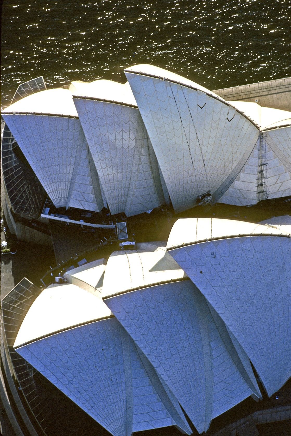 Kein Dach des 20. Jahrhunders ist diesem vergleichbar. Eigentlich hat das Opernhaus der Stadt Sydney gar kein Dach – es ist Dach. An seinem Dach wäre der Bau fast gescheitert. Der dänische Architekt Jörn Utzon hatte 1957 den Wettbewerb mit einer blossen Skizze gewonnen. Deren Verwirklichung ab 1959 forderte die damals verfügbare Bautechnik heraus. Namentlich die eleganten Dachschalen machten Kopfzerbrechen. Lochkarten-Computer rechneten

18 Monate lang an deren Krümmung herum, 44 Zeichner fixierten begleitend die Änderungen in weit über tausend Plänen. Wen wunderts: Kostenüberschreitungen waren da kein Wunder. Utzon, den die Bauherrschaft zum Start der Bauarbeiten gezwungen hatte, bevor alle technischen Probleme gelöst waren, warf 1966 schliesslich das Handtuch. Er kehrte nie mehr nach Australien zurück, nie sah er sein Werk in situ. Die wie Segel 67 Meter hoch aufragenden, mit 1,1  Million glasierten weissen Keramikfliesen verkleideten Dachflächen wurden zur Ikone der Stadt – und wohl ganz Australiens, Der Bau wird zurzeit, und noch bis 2026,  gründlich erneuert.

(Copyright Georg Gerster/Keystone)

www.georggerster.com